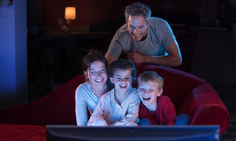 family sitting on couch watching movie on television